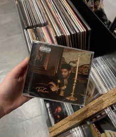 a person holding up a cd in front of a shelf full of cds and other records