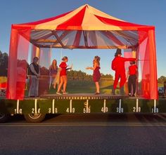 a group of people standing on the back of a truck under a red and white tent