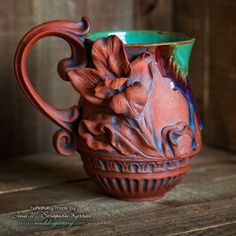 a ceramic vase with flowers on it sitting on a wooden table next to a wall