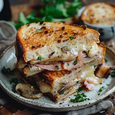 a grilled cheese sandwich on a plate with mushrooms and parsley in the background