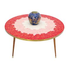 a red and white mosaic table with a blue vase on it's end stand