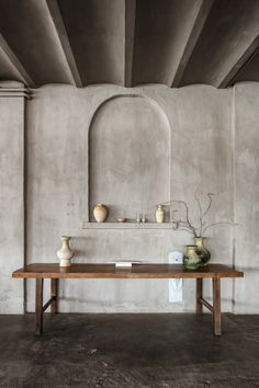 a wooden table with vases on it in front of a concrete wall and arched doorway