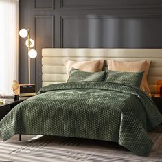 a bed with green bedspread and pillows next to a lamp on a table