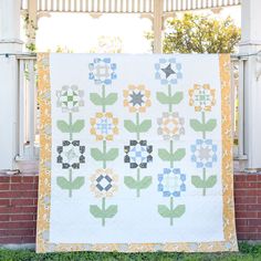 a large quilt hanging on the side of a brick wall next to a white fence