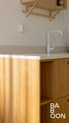 an empty kitchen with wooden cabinets and white counter tops, in front of a wall mounted shelf above the sink