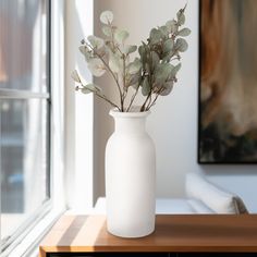 a white vase filled with flowers sitting on top of a table next to a window