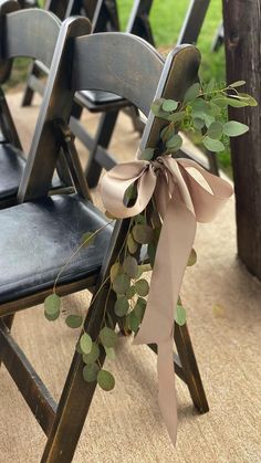 a row of wooden chairs with ribbons tied around the back of them and eucalyptus leaves on each chair