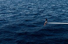 a person sitting on the edge of a boat in the middle of the ocean,