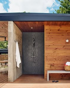 an outdoor shower with wooden walls and flooring next to a white bench under a blue sky