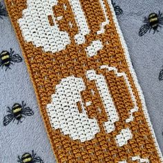 an orange and white knitted bookmark with bees on the front, one in the middle