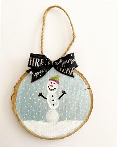 a snowman ornament hanging from a rope on a white wall with black ribbon