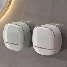 two white and gold wall mounted urinals next to a round mirror on the wall