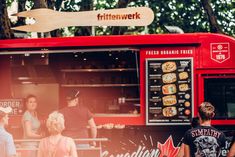 people standing in line to order food from a fast food truck that is painted red