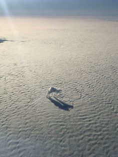 an airplane wing flying over the clouds in the sky with a heart shaped shadow on it