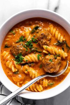 a white bowl filled with pasta and meatballs in tomato sauce, garnished with parsley