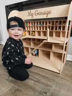 a little boy sitting on the floor next to a toy garage with toys in it