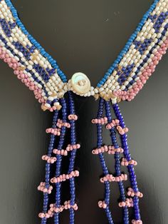 beaded necklace hanging on the wall in front of a black background with pink, white and blue beads