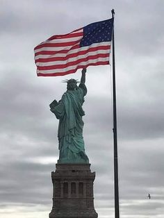 the statue of liberty is holding an american flag in front of a gray cloudy sky