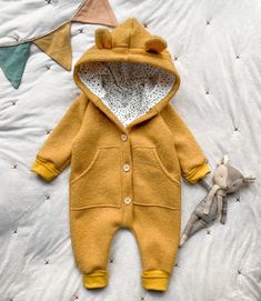 a teddy bear laying on top of a bed next to a baby's clothes