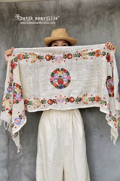 a woman holding up a piece of cloth in front of her face and wearing a straw hat