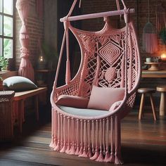 a pink hanging chair next to a window in a room with brick walls and wooden floors