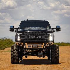 a black truck parked on top of a dirt covered field in front of a sky filled with clouds