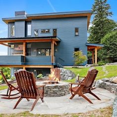 two wooden chairs sitting next to a fire pit in front of a blue house on a hill