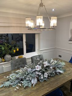 a dining room table with flowers and greenery on it, in front of a window