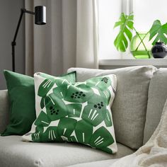 two green pillows sitting on top of a white couch next to a lamp and potted plant