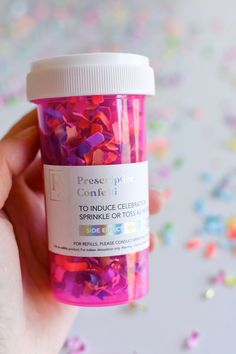 a hand holding a jar filled with pink and purple confetti