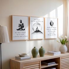 three framed pictures hang on the wall next to a table with vases and books