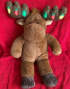 a brown stuffed moose laying on top of a red blanket with christmas lights around it's antlers