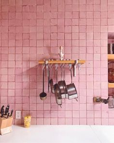 a pink brick wall with pots and pans hanging from it's hooks on the shelf