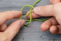 two hands are working on a piece of green string that has been knotted into a knot