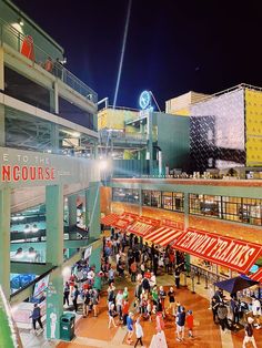 people are walking around in an indoor shopping mall at night time, with neon signs on the buildings