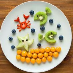 a white plate topped with kiwis, oranges and blueberries on top of a wooden table