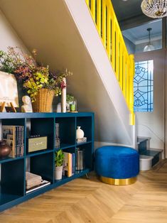 a blue ottoman sitting under a yellow stair case next to a wooden table with books on it