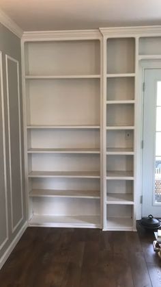 an empty room with white bookcases and wood floors