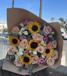 a bouquet of sunflowers and roses in a brown paper wrapper on a railing