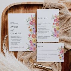 the wedding stationery is laid out on a wooden tray with flowers and greenery