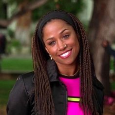 a woman with dreadlocks standing in front of a tree smiling at the camera