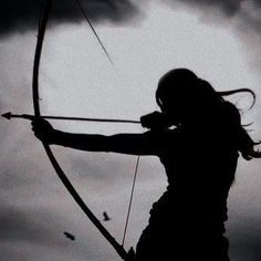 the silhouette of a woman holding a bow and arrow in front of a cloudy sky