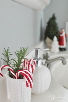 two white vases with candy canes in them sitting on a bathroom sink next to a faucet