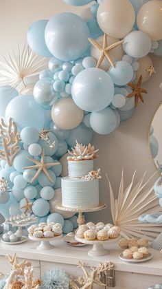 a table topped with lots of blue and white balloons next to a cake covered in starfish