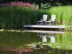 two lawn chairs sitting on a dock in the middle of a pond with lily pads