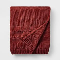 a red knitted blanket folded on top of a white table with an open end