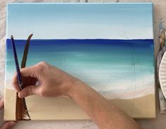 someone is painting a beach scene with blue water