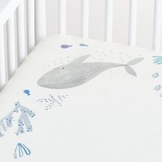 a white crib with a blue and gray whale print on the bottom sheet that is attached to it