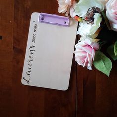 a clipboard with writing on it next to some pink flowers and a purple pen