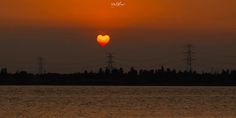 the sun is setting over water with power lines in the background